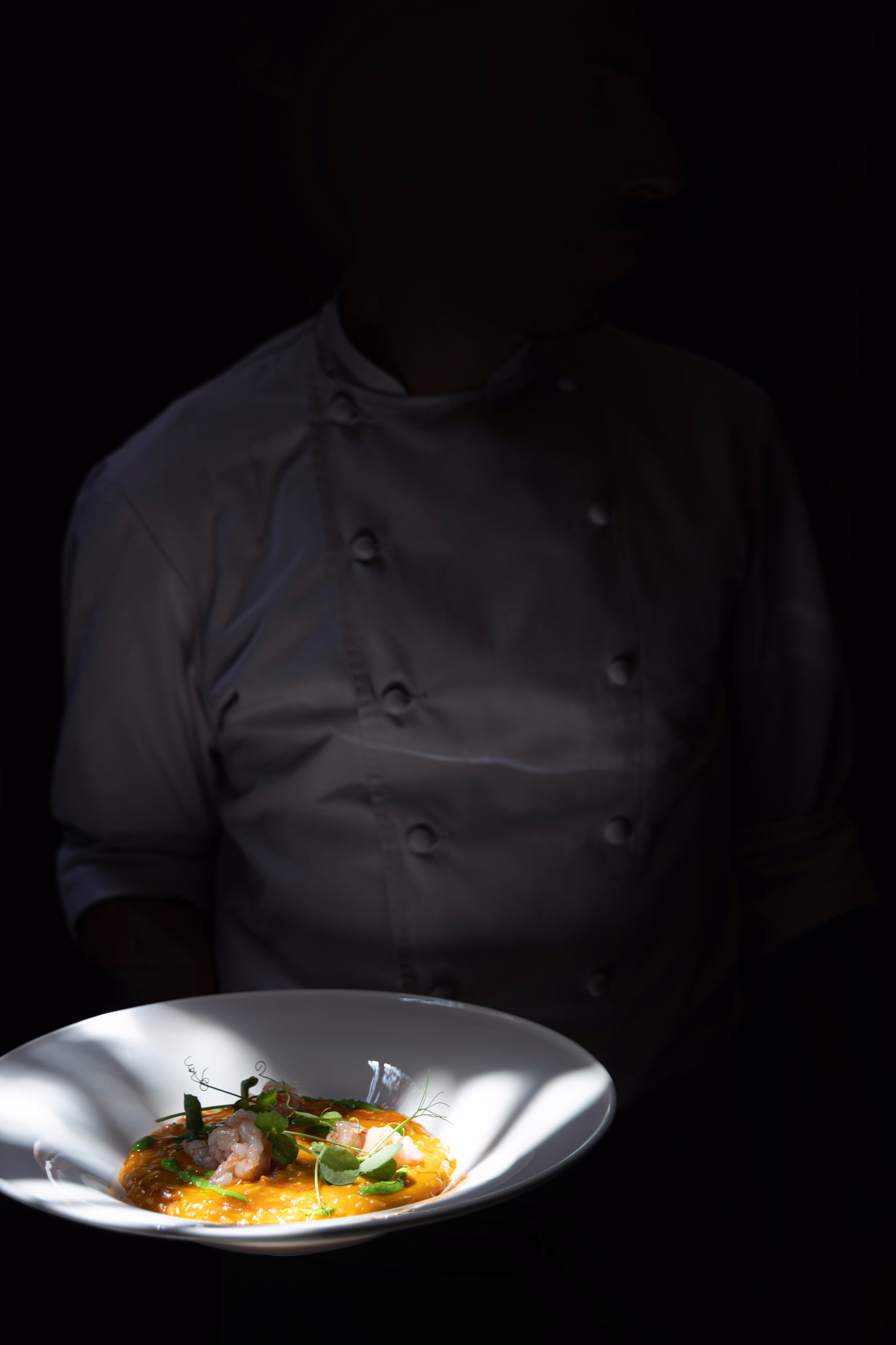 Chef holding illuminated plated dish in dark atmospheric lighting
